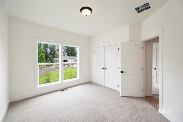 unfurnished bedroom with baseboards, visible vents, a closet, and light colored carpet