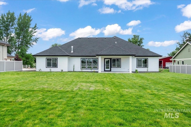 rear view of house featuring a yard, a shingled roof, and fence