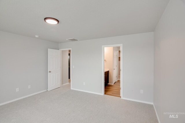 unfurnished bedroom featuring light carpet and ensuite bath