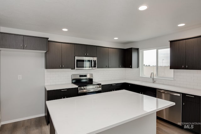 kitchen with stainless steel appliances, hardwood / wood-style flooring, a center island, and backsplash