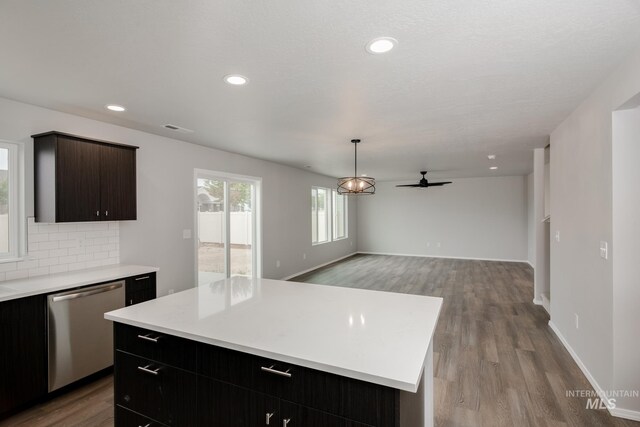 kitchen featuring decorative light fixtures, backsplash, a center island, stainless steel dishwasher, and light wood-type flooring