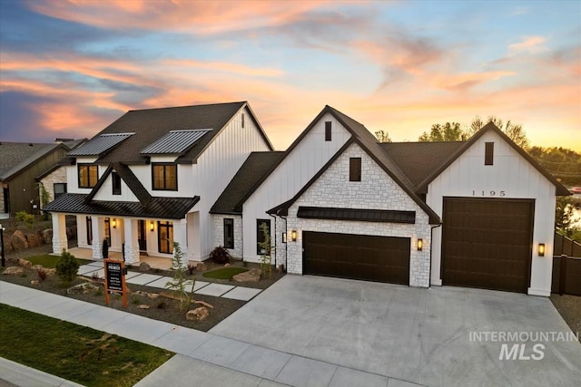 modern inspired farmhouse with an attached garage, board and batten siding, concrete driveway, a standing seam roof, and covered porch