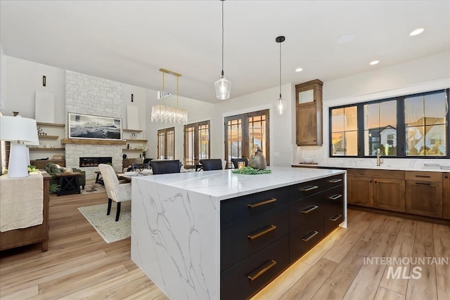 kitchen featuring brown cabinetry, light stone countertops, a center island, light wood finished floors, and decorative light fixtures