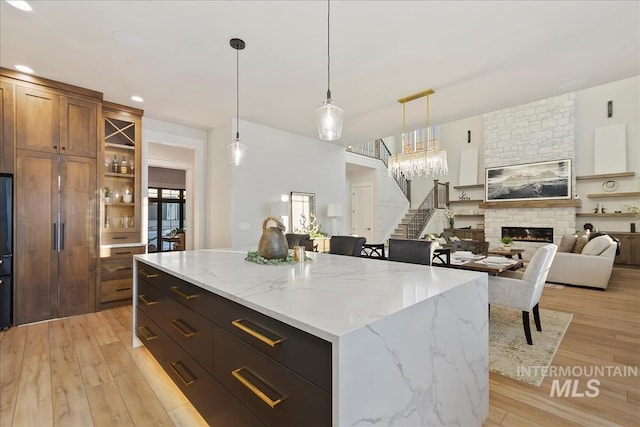 kitchen with brown cabinets, hanging light fixtures, a large fireplace, a center island, and light wood-type flooring