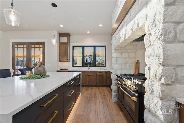 kitchen featuring french doors, double oven range, pendant lighting, light stone countertops, and light wood finished floors