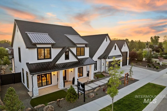 back of house at dusk with covered porch, a standing seam roof, roof with shingles, and a garage