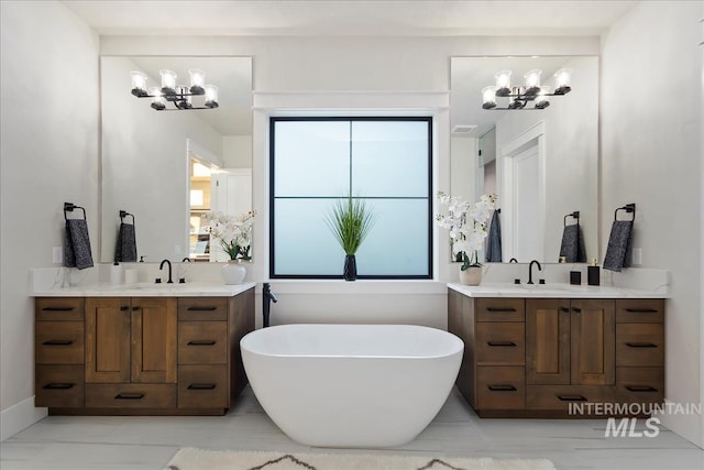 full bathroom featuring a sink, a freestanding tub, two vanities, and a notable chandelier