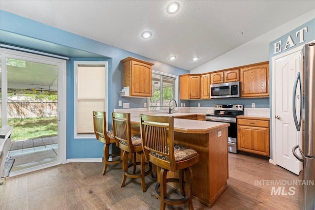 kitchen with stainless steel appliances, wood finished floors, vaulted ceiling, a kitchen breakfast bar, and light countertops