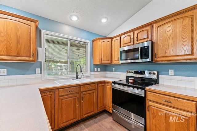 kitchen featuring stainless steel appliances, a sink, light countertops, lofted ceiling, and a textured ceiling