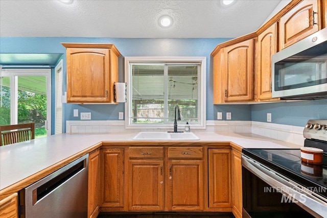 kitchen featuring stainless steel appliances, a sink, a textured ceiling, light countertops, and brown cabinetry