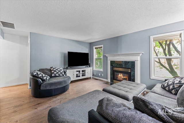 living area with wood finished floors, a high end fireplace, a textured ceiling, and baseboards