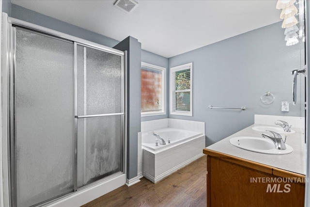 bathroom with wood finished floors, a stall shower, a garden tub, and double vanity