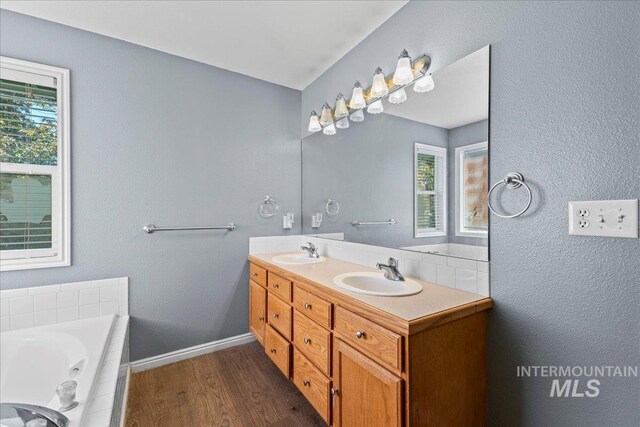 full bath with wood finished floors, double vanity, a garden tub, and baseboards