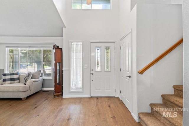 entrance foyer featuring stairway, light wood-type flooring, a high ceiling, and baseboards