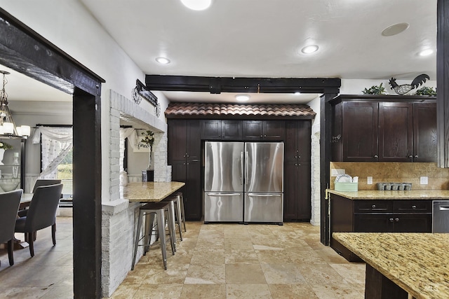 kitchen featuring backsplash, stainless steel appliances, dark brown cabinetry, light stone counters, and decorative light fixtures