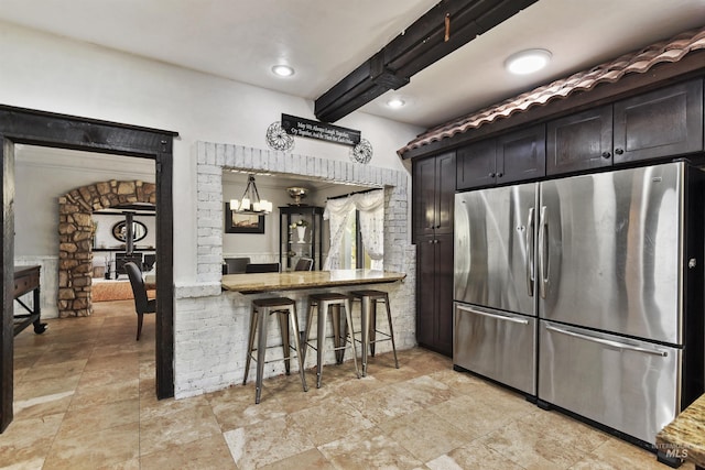 kitchen featuring a kitchen breakfast bar, stainless steel fridge, light stone counters, and beamed ceiling