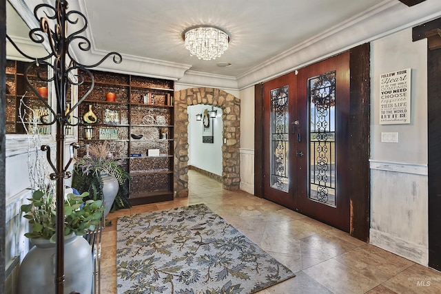 foyer entrance with a notable chandelier, crown molding, and french doors