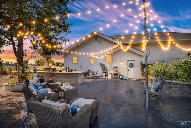 back house at dusk with a patio, exterior bar, and outdoor lounge area