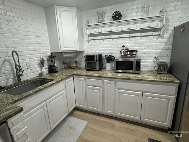 bar featuring stone countertops, sink, light hardwood / wood-style floors, white cabinets, and brick wall