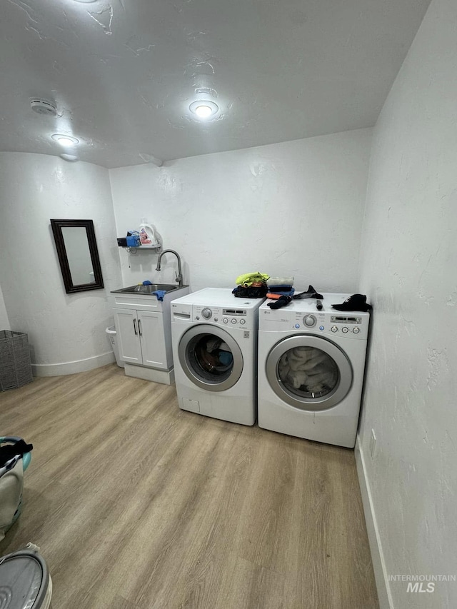 washroom featuring cabinets, sink, washer and clothes dryer, and light hardwood / wood-style flooring