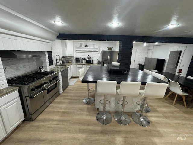 kitchen with a breakfast bar, white cabinetry, stainless steel appliances, a center island, and light hardwood / wood-style floors