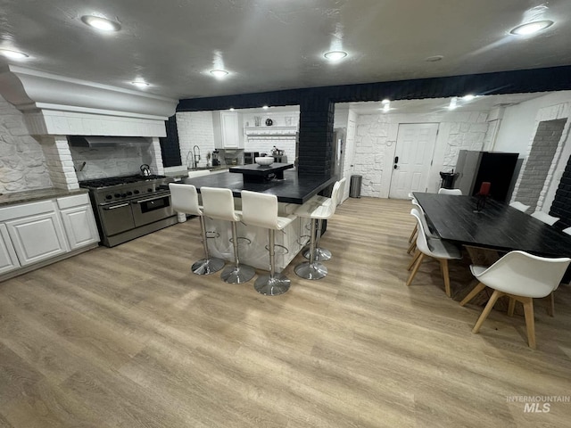 kitchen featuring a breakfast bar area, white cabinets, backsplash, range with two ovens, and light hardwood / wood-style flooring