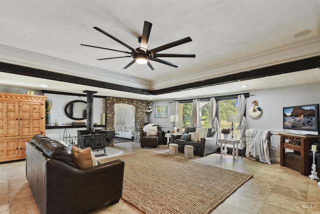 living room with crown molding, ceiling fan, a raised ceiling, and a wood stove