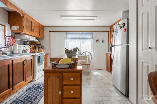 kitchen featuring freestanding refrigerator, electric range, under cabinet range hood, a sink, and brown cabinetry
