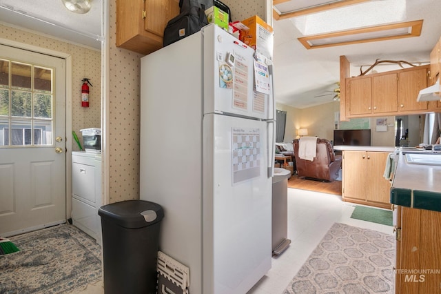 kitchen with freestanding refrigerator, washer / clothes dryer, light flooring, light countertops, and under cabinet range hood