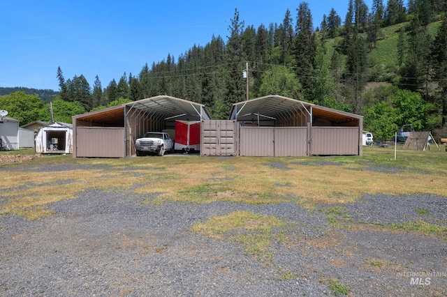 view of car parking with driveway, a carport, and a view of trees