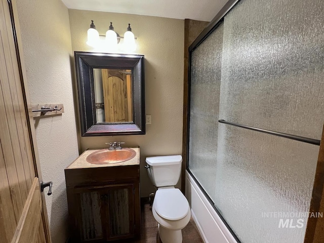13974 Rustic Rd, Mccall, ID 83638 - bathroom with toilet, vanity, a textured wall, and bath / shower combo with glass door