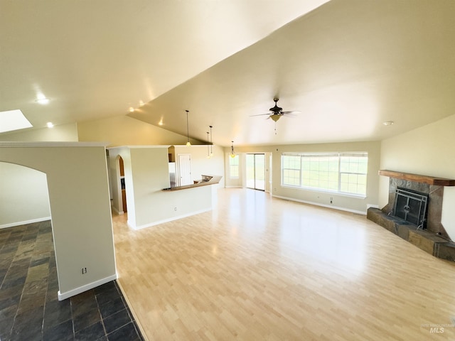 166 Eric Rd, Shoshone, ID 83352 - unfurnished living room with arched walkways, a tiled fireplace, a ceiling fan, vaulted ceiling, and baseboards