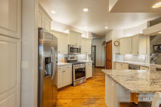 kitchen featuring stainless steel appliances, light stone counters, a kitchen bar, decorative backsplash, and kitchen peninsula