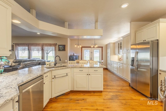 kitchen with sink, light hardwood / wood-style flooring, appliances with stainless steel finishes, light stone countertops, and decorative light fixtures