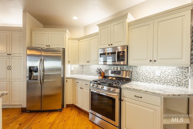 kitchen featuring appliances with stainless steel finishes, light hardwood / wood-style floors, light stone countertops, cream cabinets, and backsplash