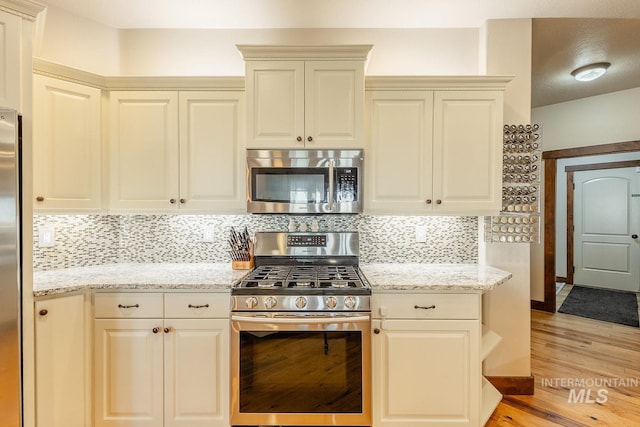 kitchen with light hardwood / wood-style flooring, stainless steel appliances, light stone countertops, cream cabinets, and decorative backsplash