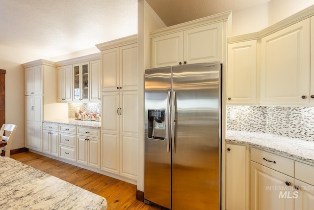 kitchen with light hardwood / wood-style flooring, stainless steel fridge, backsplash, light stone countertops, and cream cabinetry