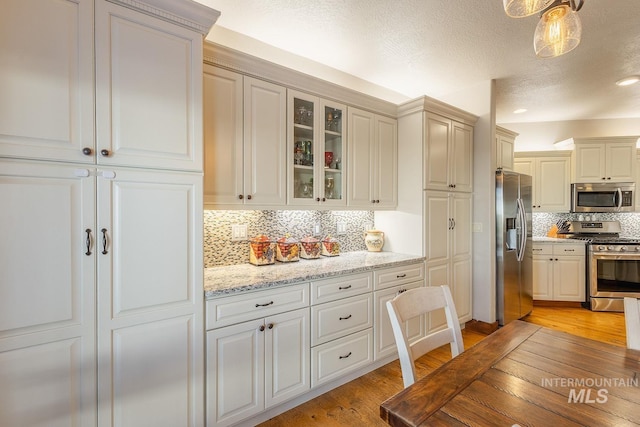 kitchen with decorative backsplash, hanging light fixtures, light stone counters, stainless steel appliances, and light wood-type flooring