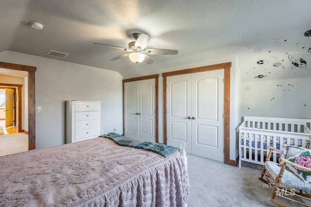 bedroom featuring multiple closets, ceiling fan, carpet, and a textured ceiling