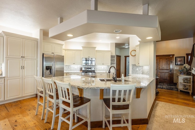 kitchen with appliances with stainless steel finishes, a kitchen breakfast bar, light stone counters, kitchen peninsula, and light hardwood / wood-style flooring