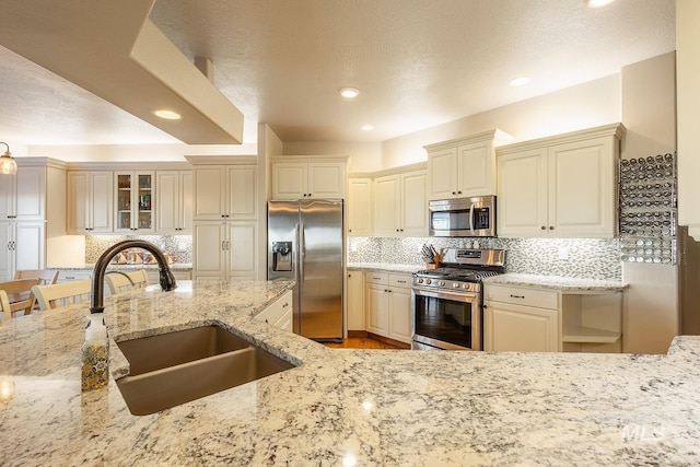 kitchen featuring sink, appliances with stainless steel finishes, light stone countertops, decorative backsplash, and cream cabinetry