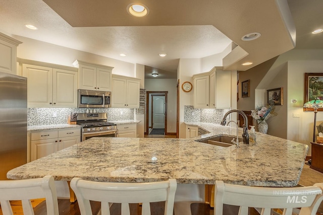 kitchen featuring cream cabinets, stainless steel appliances, kitchen peninsula, and sink