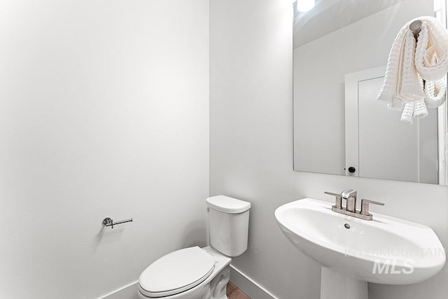 half bathroom featuring a sink, toilet, baseboards, and wood finished floors