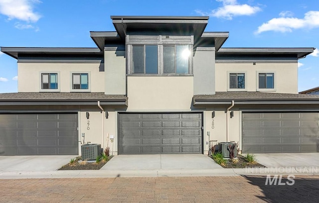 view of front of home with a garage, stucco siding, central AC, and driveway