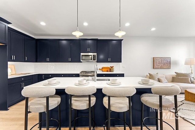 kitchen featuring stainless steel microwave, a sink, light countertops, a kitchen breakfast bar, and decorative backsplash