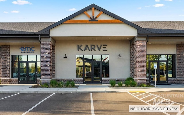 entrance to property with french doors, brick siding, a shingled roof, and uncovered parking