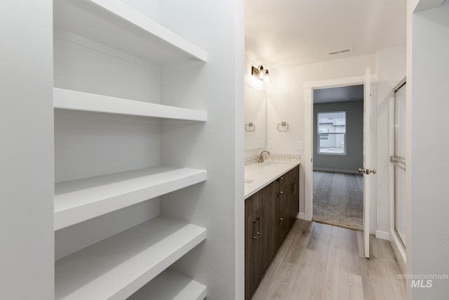full bath with a shower stall, a sink, double vanity, visible vents, and wood finished floors