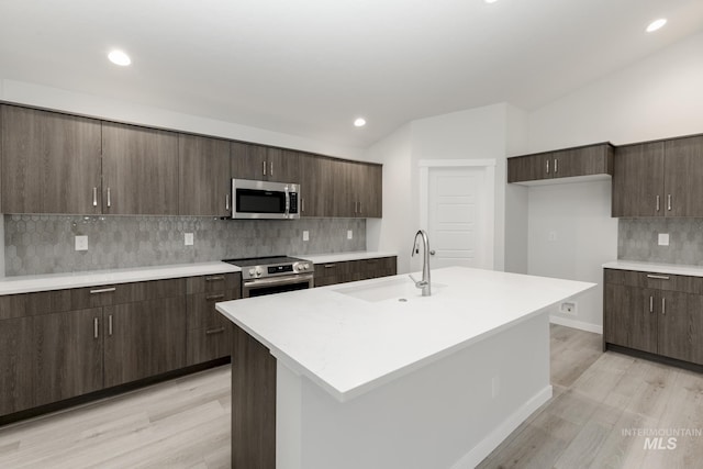 kitchen with a sink, appliances with stainless steel finishes, light countertops, light wood finished floors, and backsplash