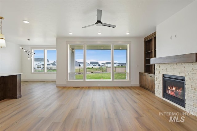 unfurnished living room featuring a wealth of natural light, a fireplace, light hardwood / wood-style flooring, and built in shelves