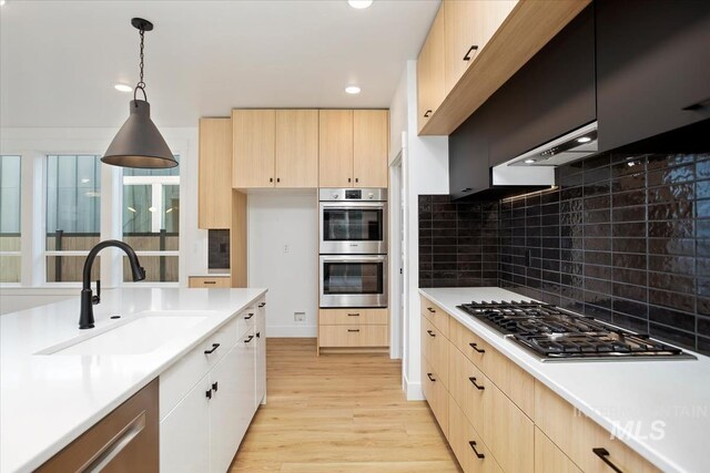 kitchen featuring appliances with stainless steel finishes, backsplash, light brown cabinets, pendant lighting, and sink